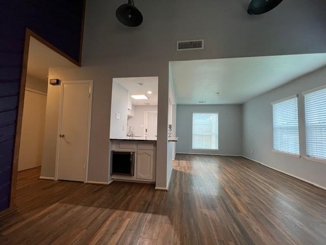 unfurnished living room with dark wood-style floors, visible vents, and a sink