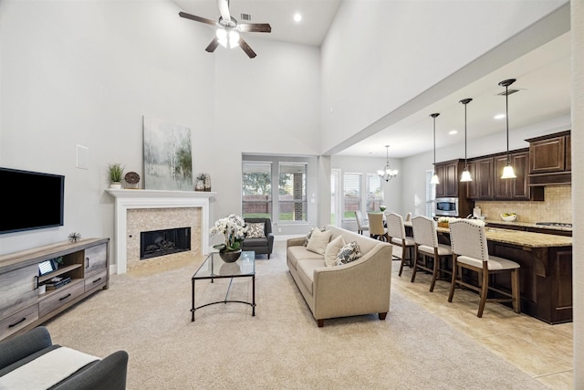 living area with baseboards, a tile fireplace, a high ceiling, ceiling fan with notable chandelier, and recessed lighting