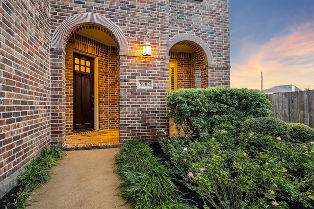 doorway to property with brick siding and fence