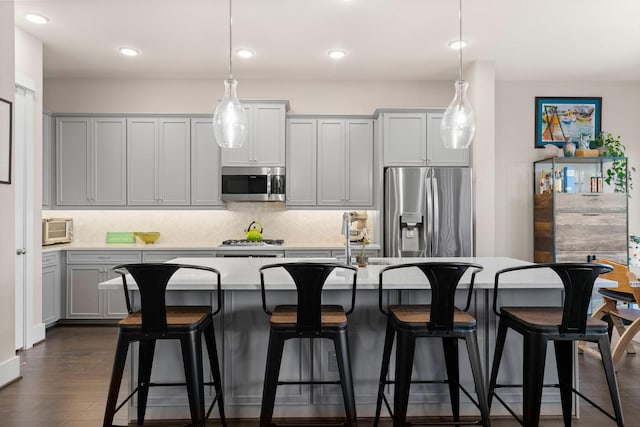 kitchen featuring a center island with sink, dark wood finished floors, decorative light fixtures, stainless steel appliances, and backsplash