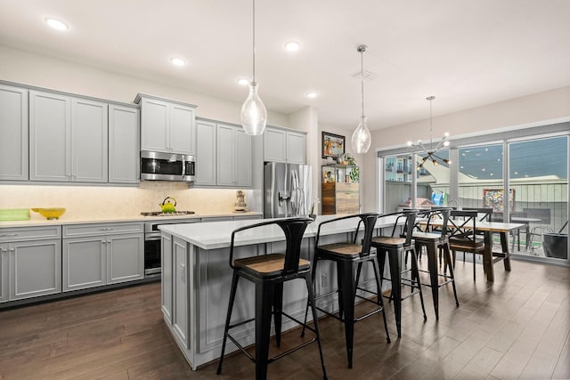 kitchen with a breakfast bar area, gray cabinets, decorative backsplash, appliances with stainless steel finishes, and dark wood-type flooring