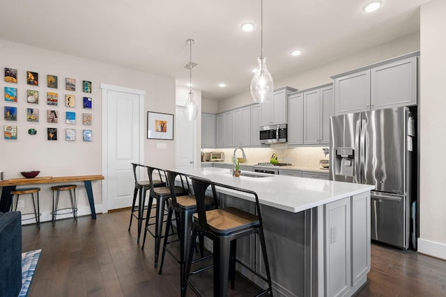 kitchen featuring stainless steel appliances, dark wood-style flooring, a sink, and a kitchen breakfast bar