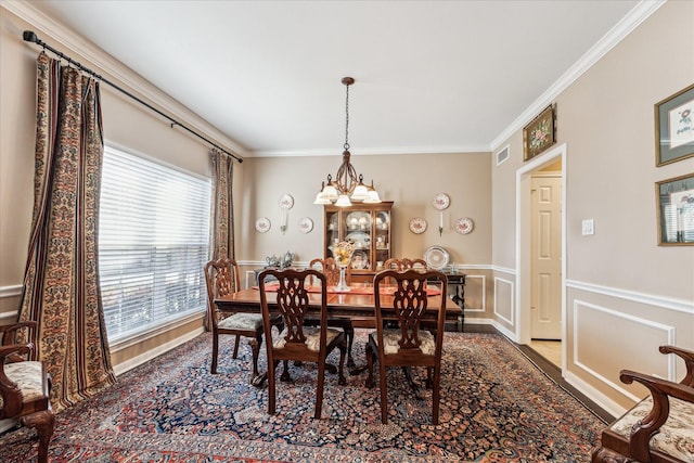 dining room with a chandelier, a decorative wall, visible vents, ornamental molding, and wainscoting