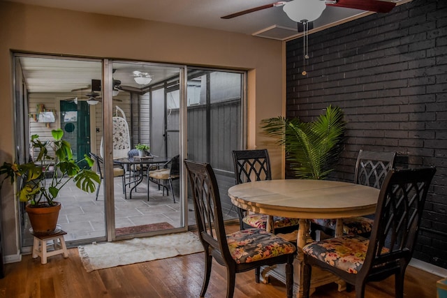 dining space with a ceiling fan, wood finished floors, and brick wall