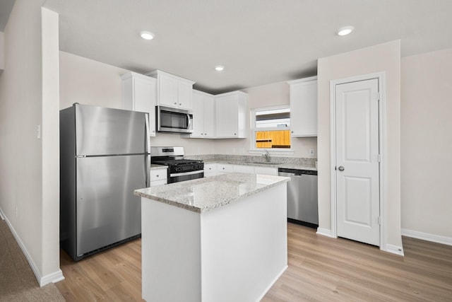 kitchen with white cabinets, a kitchen island, light stone counters, appliances with stainless steel finishes, and a sink