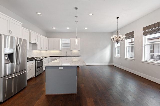 kitchen with a sink, a kitchen island, baseboards, appliances with stainless steel finishes, and tasteful backsplash