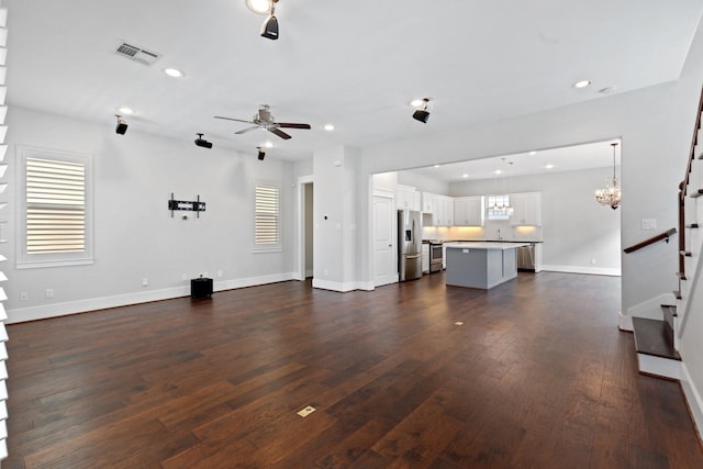 unfurnished living room with dark wood finished floors, visible vents, stairway, baseboards, and ceiling fan with notable chandelier