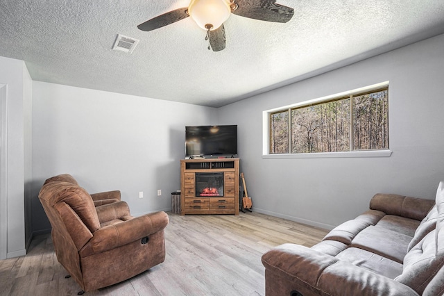 living area featuring ceiling fan, visible vents, wood finished floors, and a glass covered fireplace