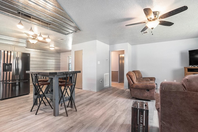 dining room featuring light wood finished floors, visible vents, a textured ceiling, and a ceiling fan