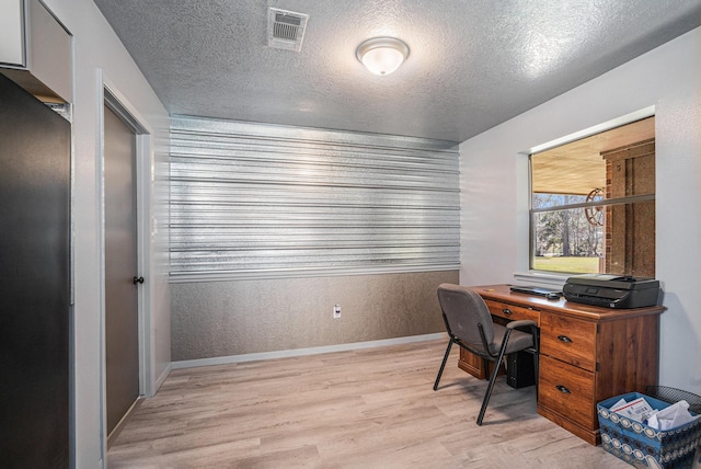 office space featuring visible vents, baseboards, light wood-style floors, a textured wall, and a textured ceiling