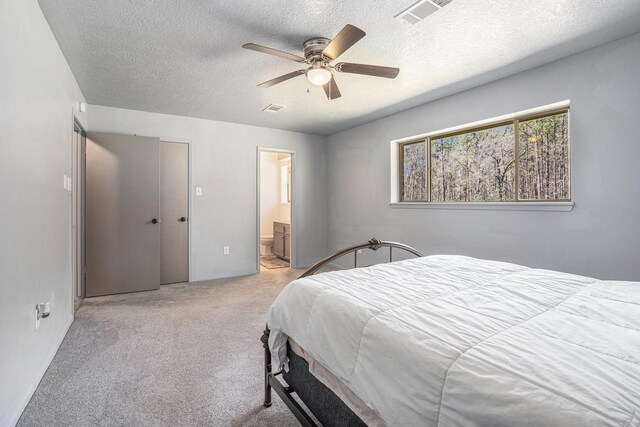 bedroom with visible vents, light carpet, ensuite bathroom, a ceiling fan, and a textured ceiling