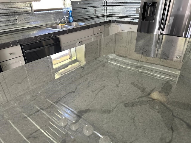 kitchen with dark stone counters, freestanding refrigerator, a sink, black dishwasher, and white cabinetry