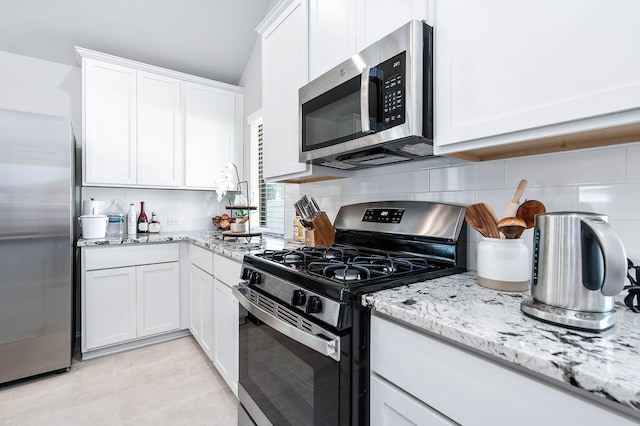 kitchen with tasteful backsplash, appliances with stainless steel finishes, white cabinets, and light stone counters