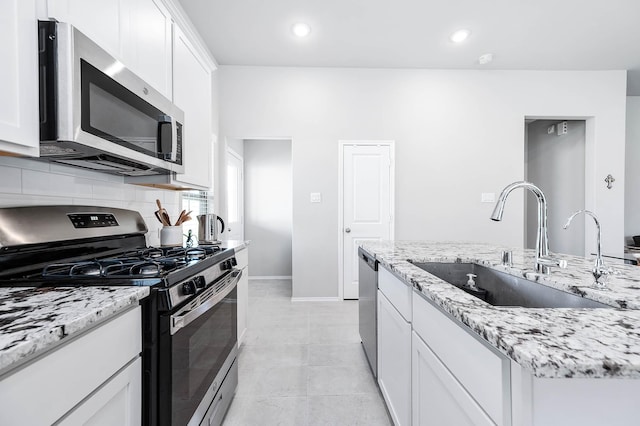 kitchen with light stone counters, stainless steel appliances, decorative backsplash, white cabinetry, and a sink