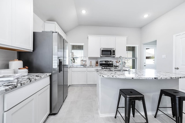 kitchen featuring light stone counters, a breakfast bar, stainless steel appliances, white cabinets, and a sink