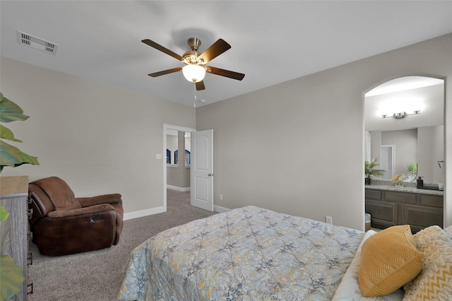 carpeted bedroom with arched walkways, a ceiling fan, visible vents, baseboards, and ensuite bath