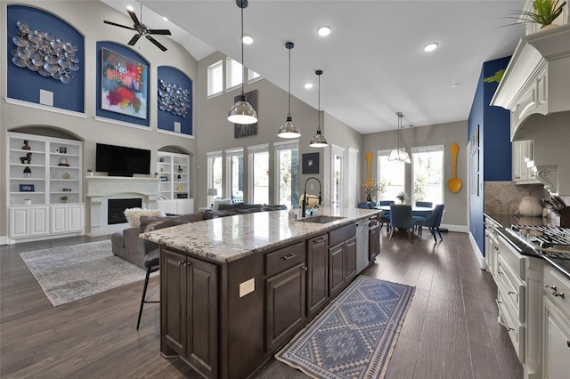 kitchen featuring light stone counters, a fireplace, dark wood-type flooring, a sink, and dark brown cabinets