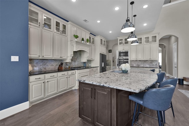 kitchen with dark wood-style floors, arched walkways, stainless steel appliances, visible vents, and a large island with sink