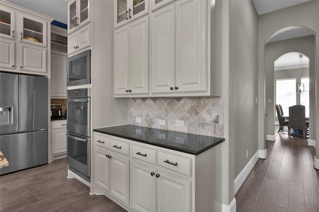 kitchen with stainless steel appliances, arched walkways, dark wood finished floors, and tasteful backsplash