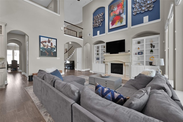 living area with arched walkways, dark wood-style flooring, a glass covered fireplace, and stairs