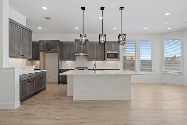 kitchen featuring light wood-style flooring, a sink, visible vents, light countertops, and stainless steel microwave