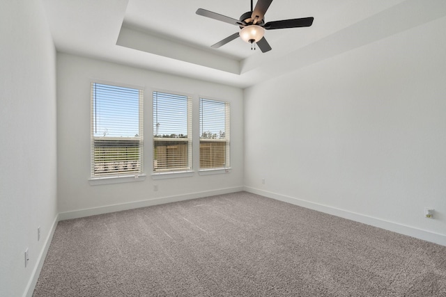 spare room with baseboards, ceiling fan, a tray ceiling, and light colored carpet