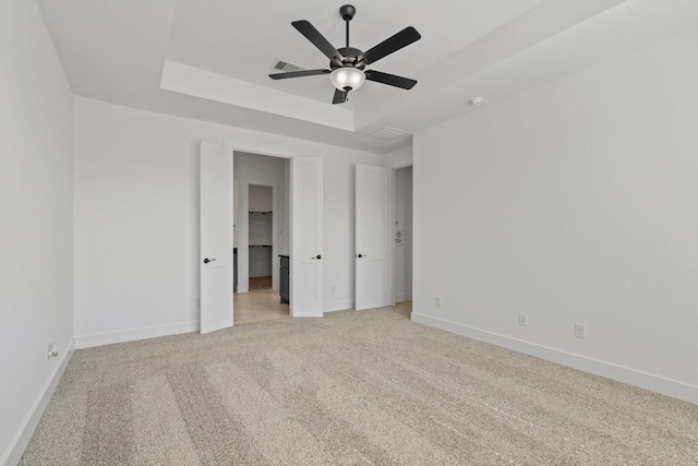 unfurnished bedroom featuring light carpet, baseboards, visible vents, a raised ceiling, and a ceiling fan