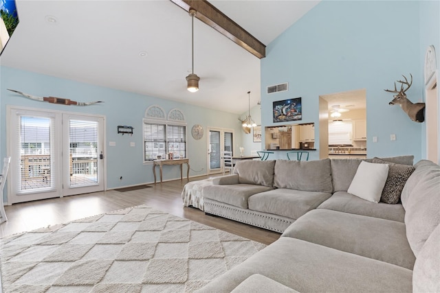 living room featuring visible vents, wood finished floors, beamed ceiling, baseboards, and ceiling fan with notable chandelier