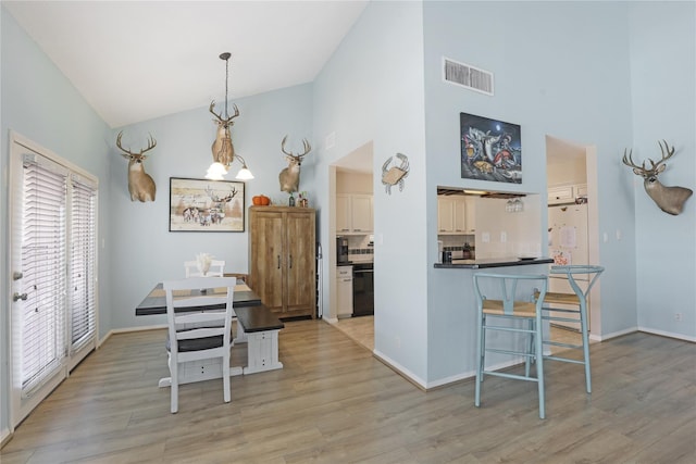 dining space featuring high vaulted ceiling, a chandelier, visible vents, and light wood finished floors