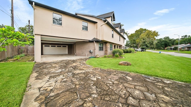 exterior space featuring driveway, a garage, a lawn, fence, and stucco siding