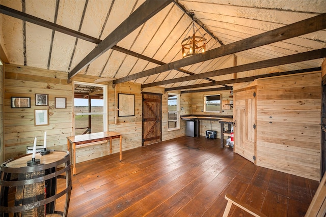 interior space with vaulted ceiling with beams, a barn door, dark wood-style flooring, wood walls, and a healthy amount of sunlight