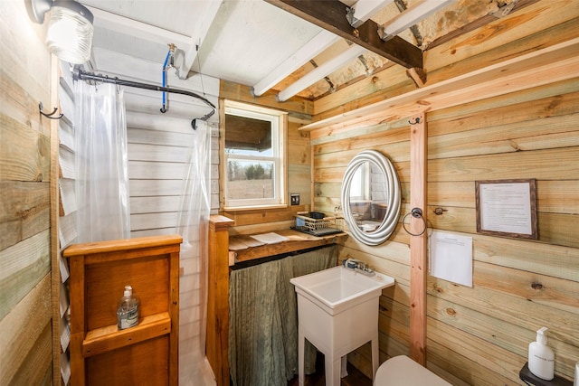 bathroom with curtained shower, toilet, wood walls, a sink, and beam ceiling