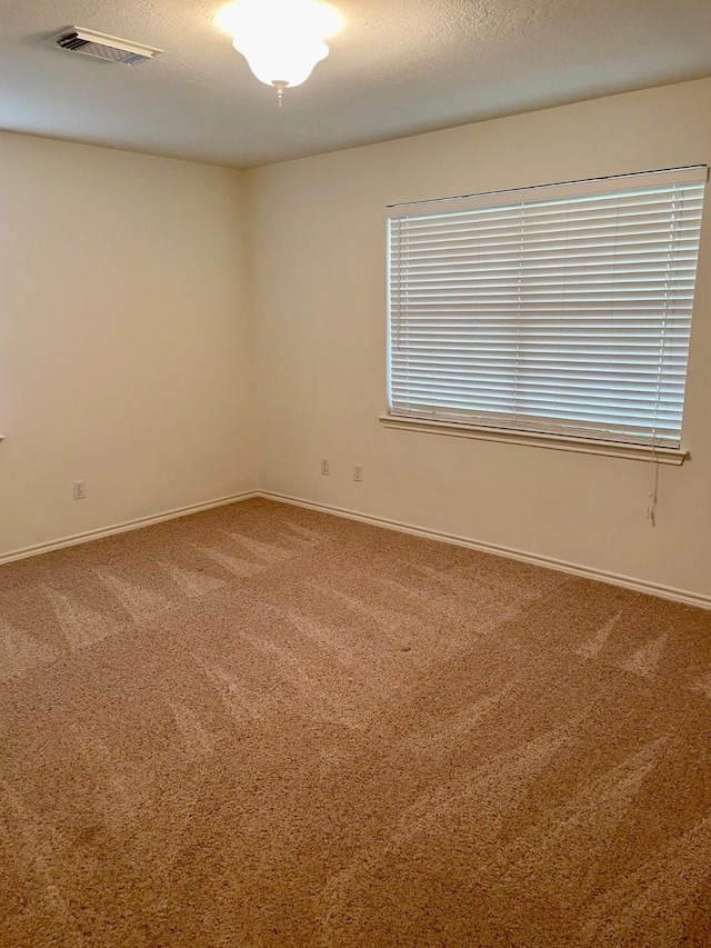 spare room featuring carpet floors, visible vents, a textured ceiling, and baseboards