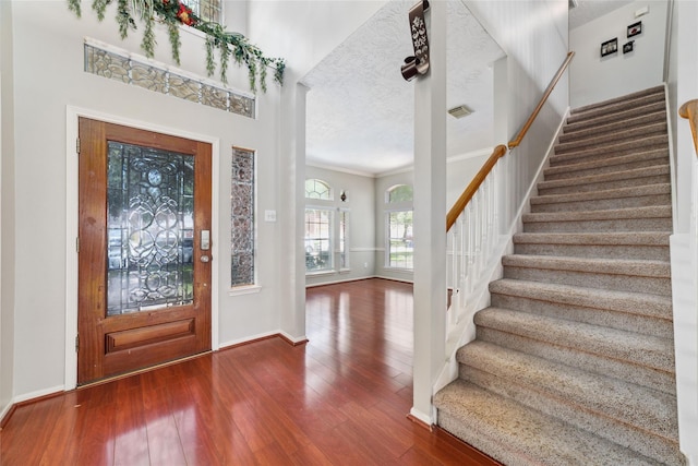 entryway with crown molding, wood-type flooring, a textured ceiling, baseboards, and stairs