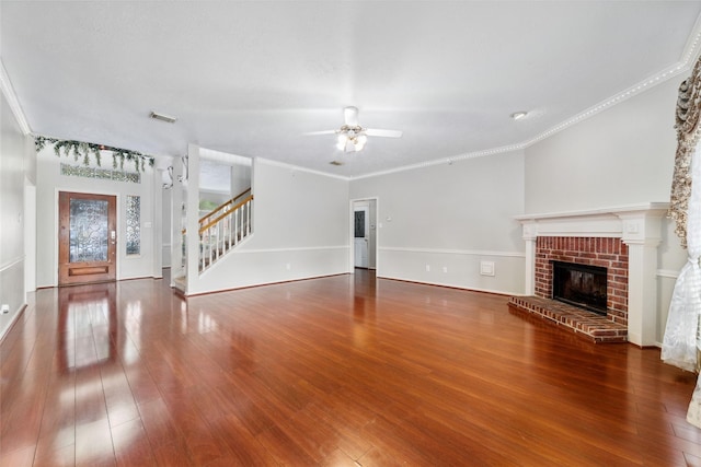 unfurnished living room featuring visible vents, stairway, ornamental molding, wood finished floors, and a brick fireplace