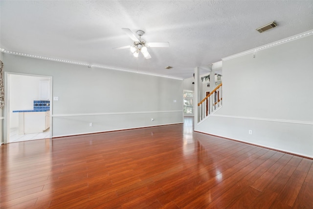 unfurnished living room featuring visible vents, hardwood / wood-style flooring, ceiling fan, stairway, and a textured ceiling