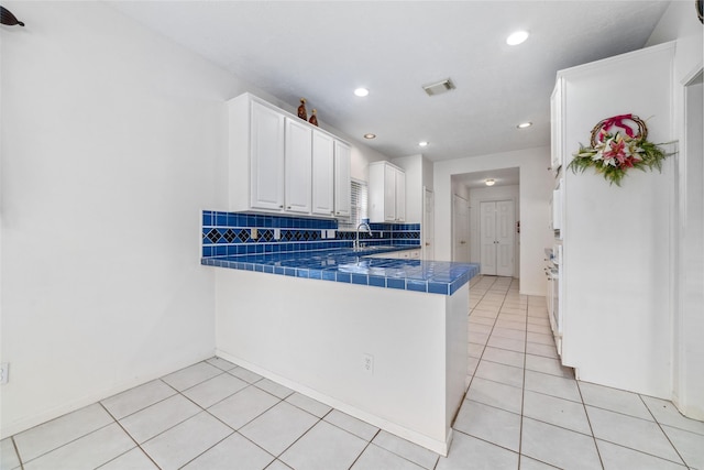 kitchen with light tile patterned floors, a peninsula, white cabinets, tile counters, and decorative backsplash