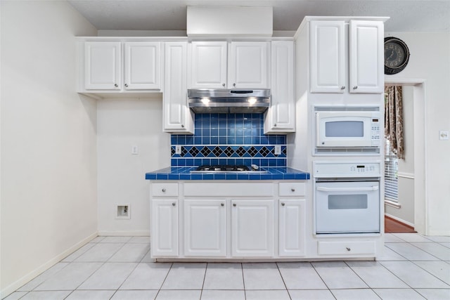 kitchen featuring tile countertops, light tile patterned floors, white cabinets, white appliances, and under cabinet range hood