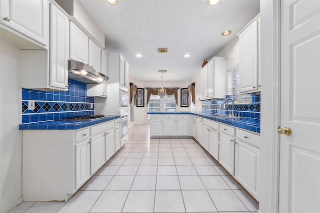 kitchen with white appliances, tile counters, a peninsula, under cabinet range hood, and a sink