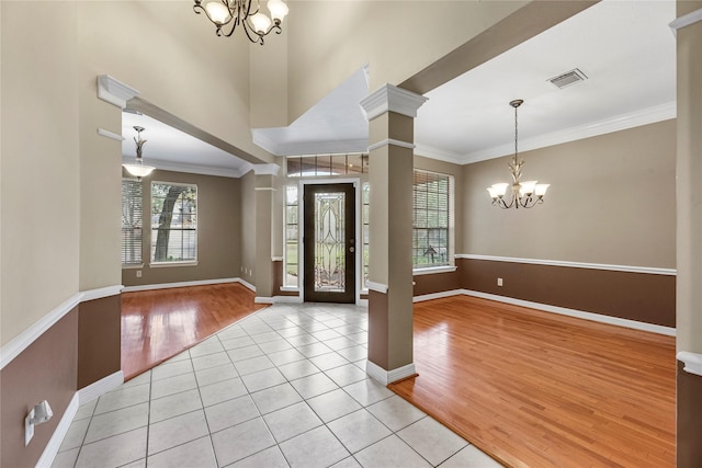 foyer entrance featuring visible vents, light wood-style flooring, decorative columns, ornamental molding, and a chandelier