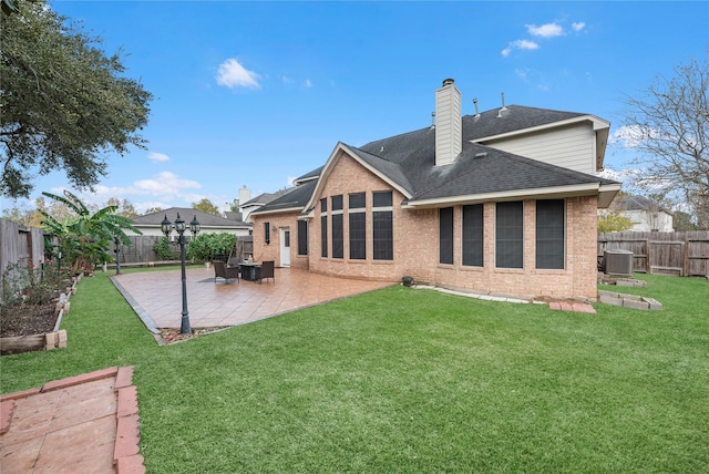 rear view of property with a lawn, a fenced backyard, brick siding, a chimney, and a patio area