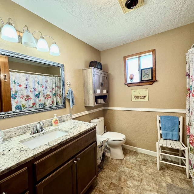 bathroom featuring baseboards, a textured wall, toilet, a textured ceiling, and vanity