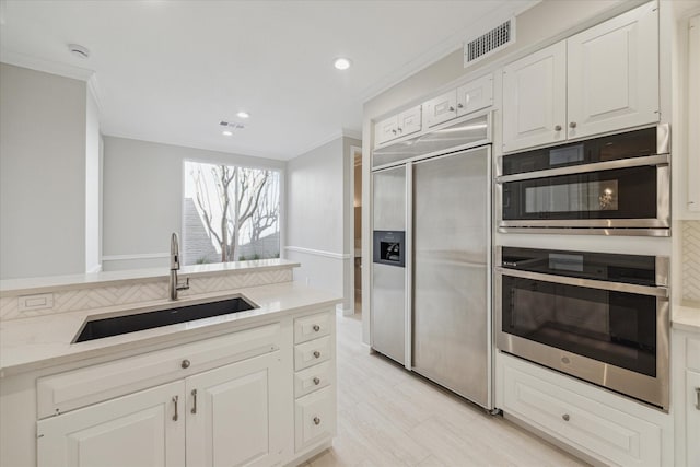 kitchen with double oven, built in fridge, a sink, visible vents, and white cabinets