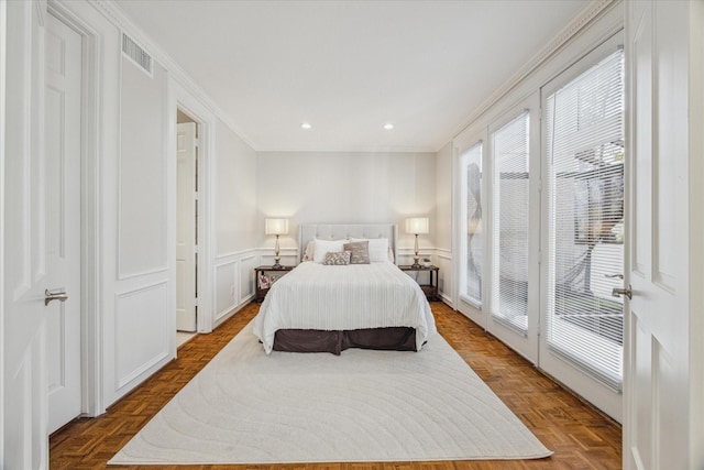 bedroom with ornamental molding, wainscoting, visible vents, and a decorative wall