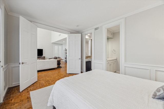 bedroom featuring crown molding, ensuite bathroom, visible vents, and a decorative wall