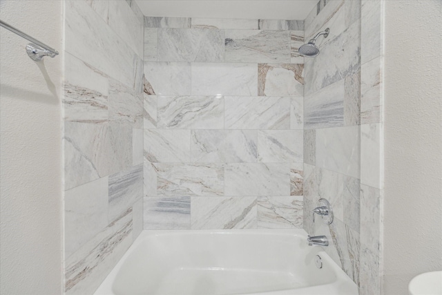 bathroom with tub / shower combination and a textured wall