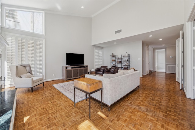 living area with recessed lighting, a high ceiling, visible vents, baseboards, and crown molding