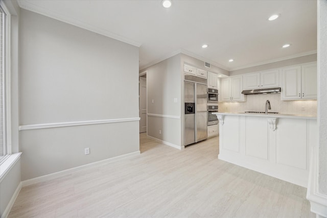 kitchen with built in fridge, under cabinet range hood, a peninsula, backsplash, and a kitchen bar