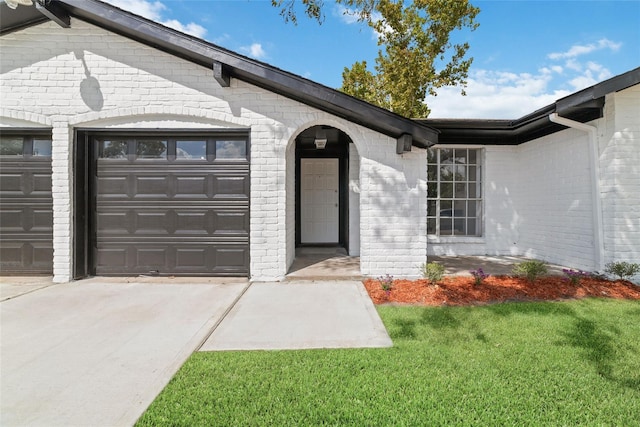 view of exterior entry featuring a garage, driveway, a lawn, and brick siding