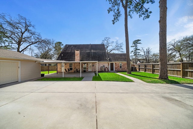 view of front of property featuring brick siding, fence, concrete driveway, a front lawn, and a chimney